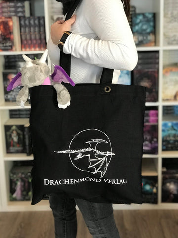 Das Produktbild zeigt einen schwarzen Leinenbeutel, auf dem mittig in weiß das Verlagslogo (ein fliegender Drache vor einem Vollmond) abgebildet ist. Darunter steht in weißen Großbuchstaben "Drachenmond Verlag".